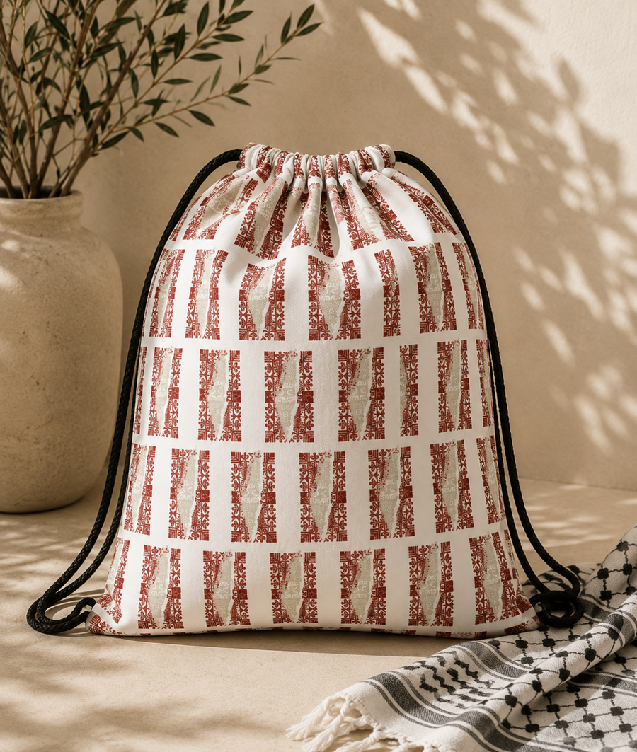 A drawstring bag with a white base and terracotta red vertical stripe pattern, styled on a beige surface with a potted plant and a black-and-white patterned scarf in a warm, sunlit setting.