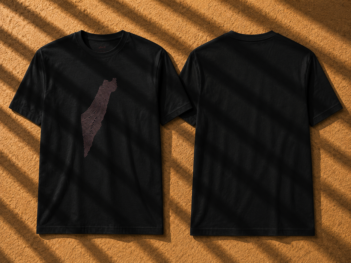 Two black short-sleeve T-shirts shown flat against a textured tan background with diagonal shadow overlays. The front shirt has a subtle dark mauve-brown silhouette graphic on the left chest, and the back shirt is plain.