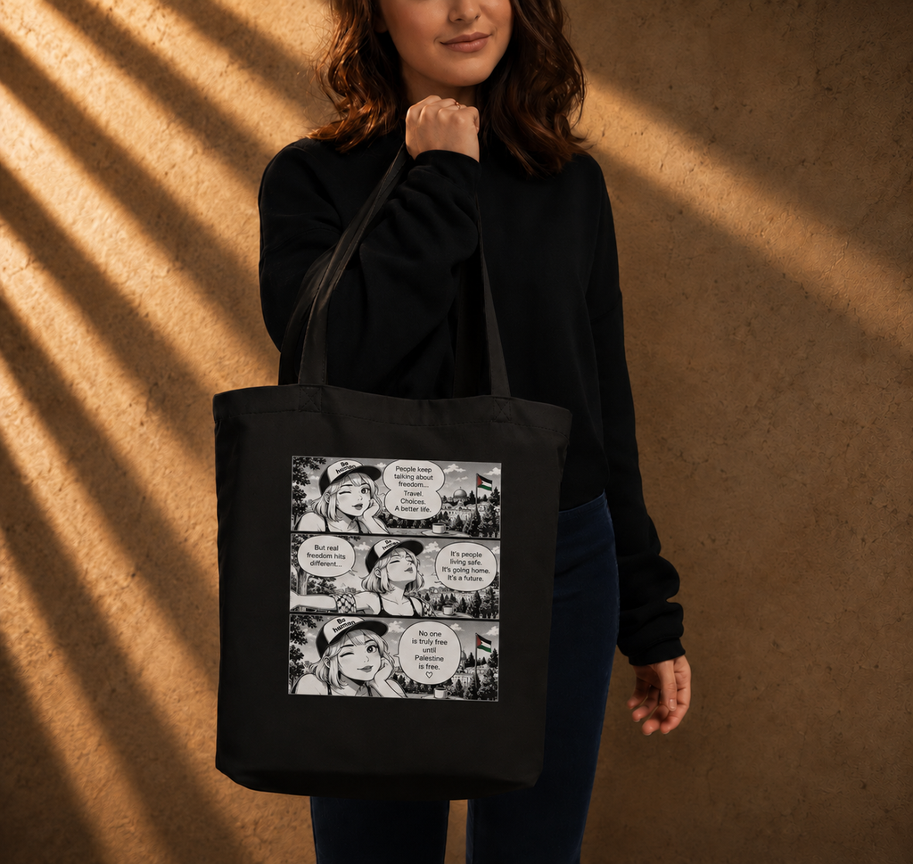 A woman wearing a black sweatshirt and dark pants carries a black canvas tote bag with a black-and-white comic strip graphic on the front, standing against a warm brown textured wall with dramatic diagonal shadows.