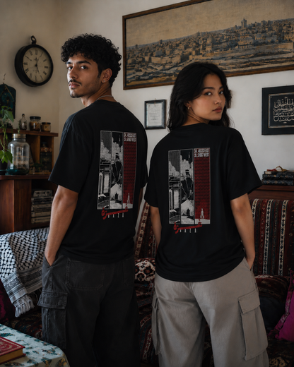 Two models standing in a room, both wearing black graphic t-shirts with a large back print featuring a black and white architectural scene with red accents and the coordinates of Gaza