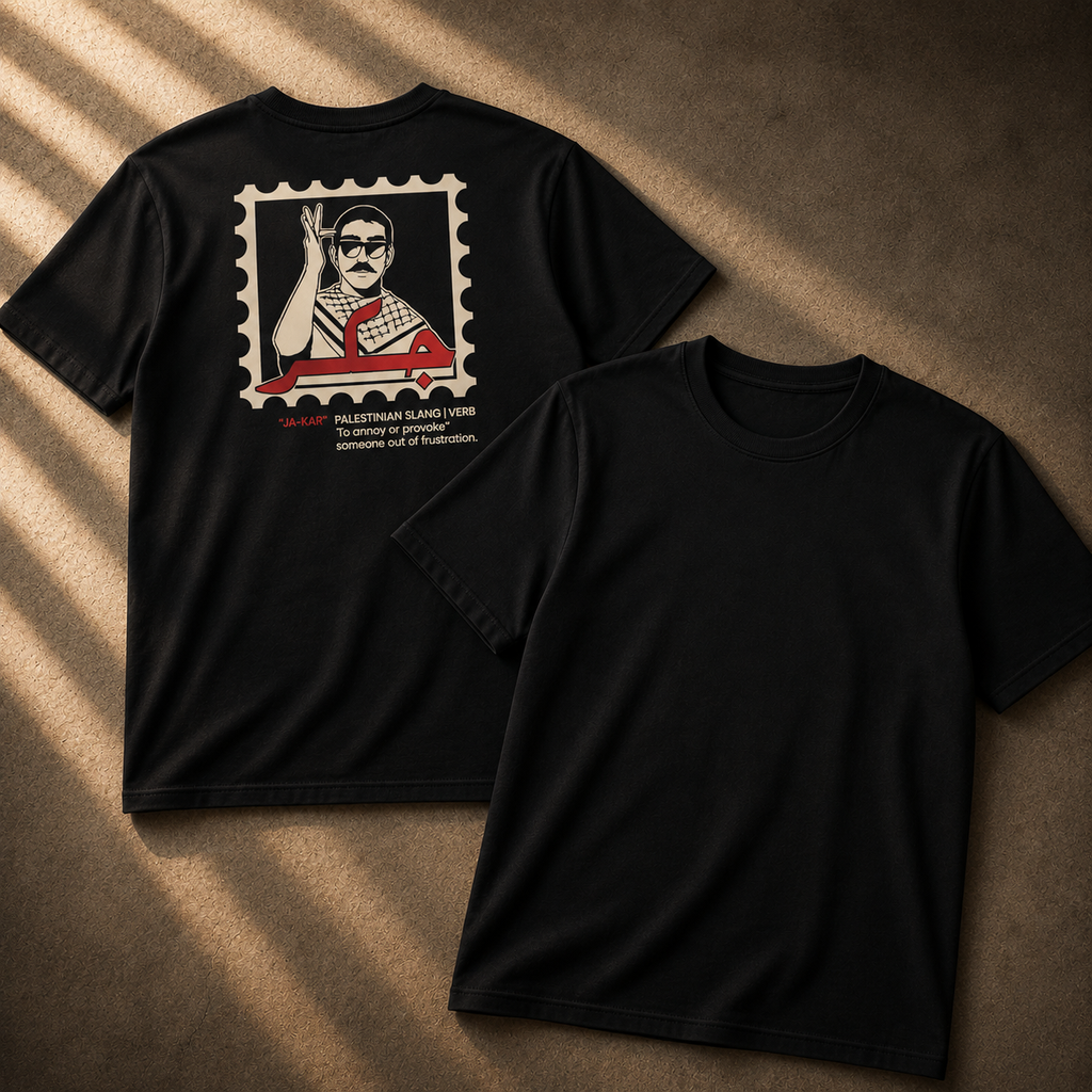 A close-up of a black t-shirt featuring a graphic print of a postage stamp. The stamp contains a stylized illustration of a man raising his hand, with red Arabic calligraphy and the text '*JA-KAR' 'PALESTINIAN SLANG | VERB To annoy or provoke someone out of spite.