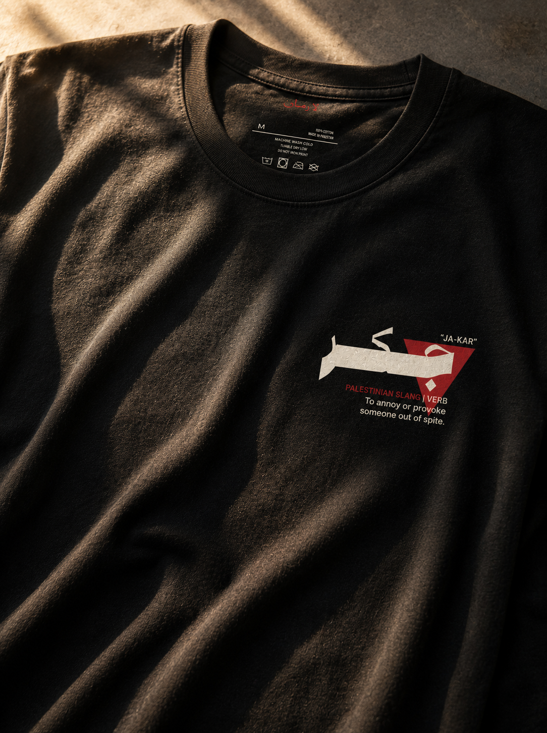 A close-up of a black crewneck t-shirt with a graphic on the left chest. The graphic features a white silhouette of a person with a dog on a leash, a red triangular shape, and the text 'J.