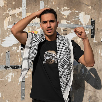 Kuffiyeh Unveiled Eyes Tshirt | handsome arab young man wearing kuffiyeh on shoulders with one hand on head and other raising fist. image for upper half only. background old cracked wall with some torn plain posters and torn out duct-tape. The image should be appealing for genz
