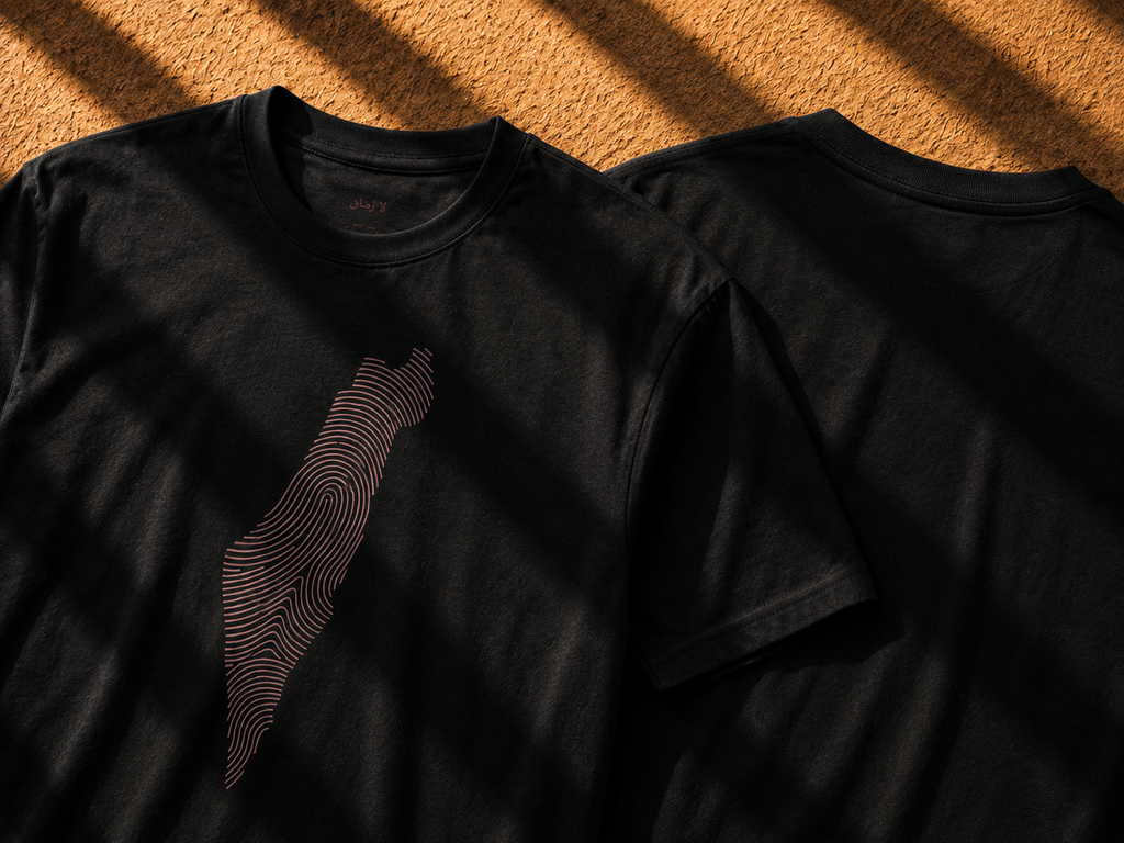 Two black short-sleeve crewneck t-shirts displayed on a textured orange-brown surface under dramatic diagonal shadows. The front shirt features a graphic of the island of Taiwan rendered in concentric wavy lines.