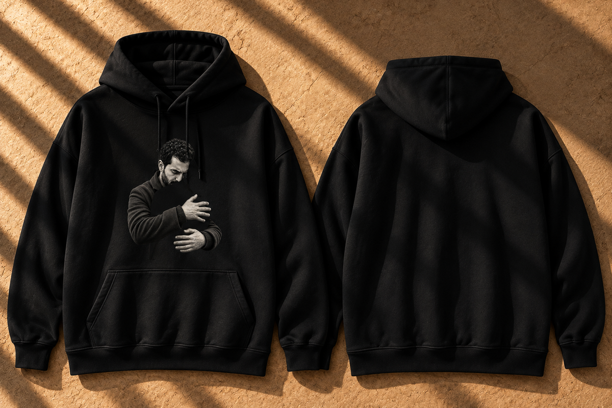 Two black pullover hoodies shown flat against a textured tan background with diagonal shadows. The left hoodie shows a grayscale printed portrait of a man on the front, and the right hoodie shows the plain back.