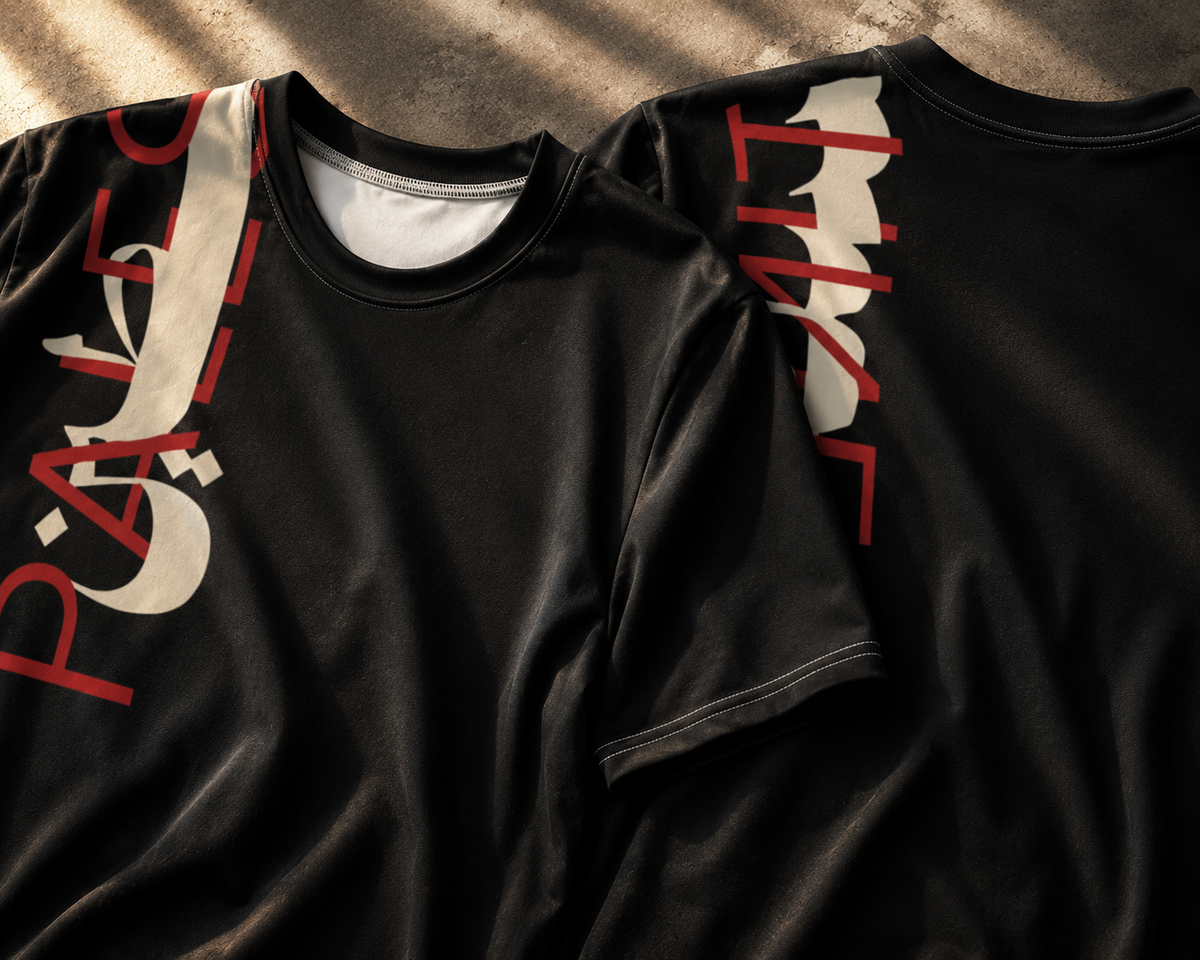 Two black short-sleeve T-shirts laid flat on a textured concrete surface, featuring large white and red graphic lettering on the sleeves.