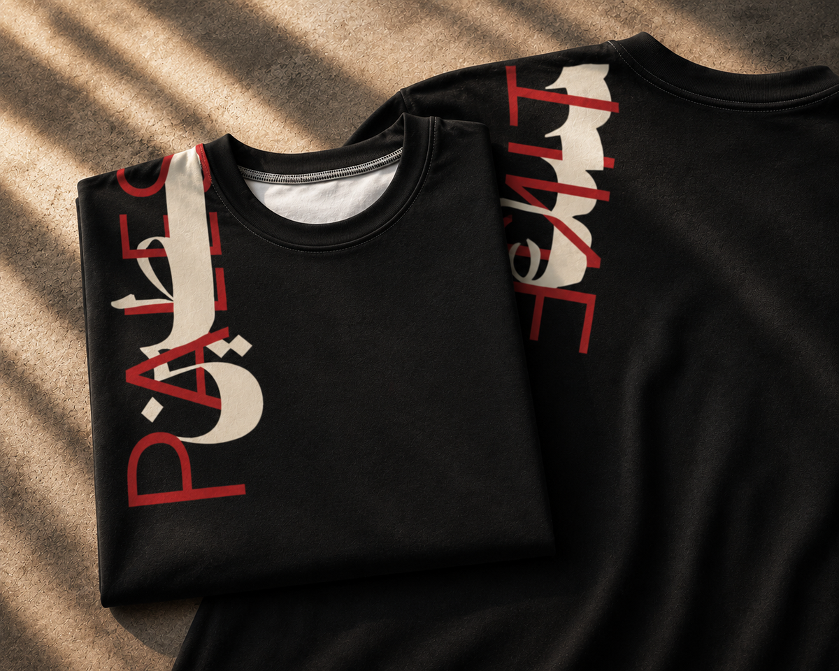 A folded black crewneck sweatshirt with a large vertical graphic print in red and off-white, layered over another black sweatshirt on a textured beige surface with diagonal shadows.
