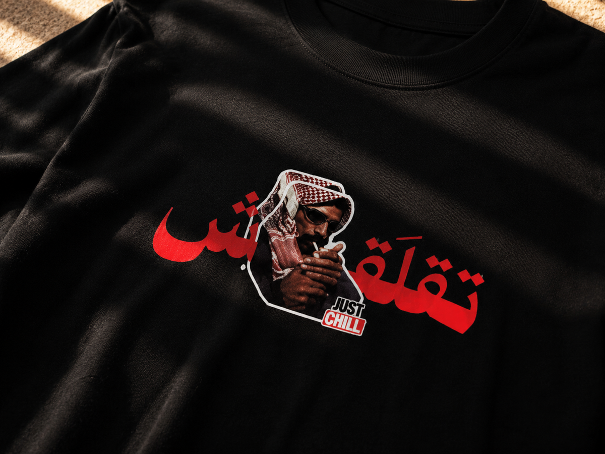 A close-up of a black t-shirt featuring a graphic print with red Arabic calligraphy, a portrait of a man in a keffiyeh, and the text 'JUST CHILL'.