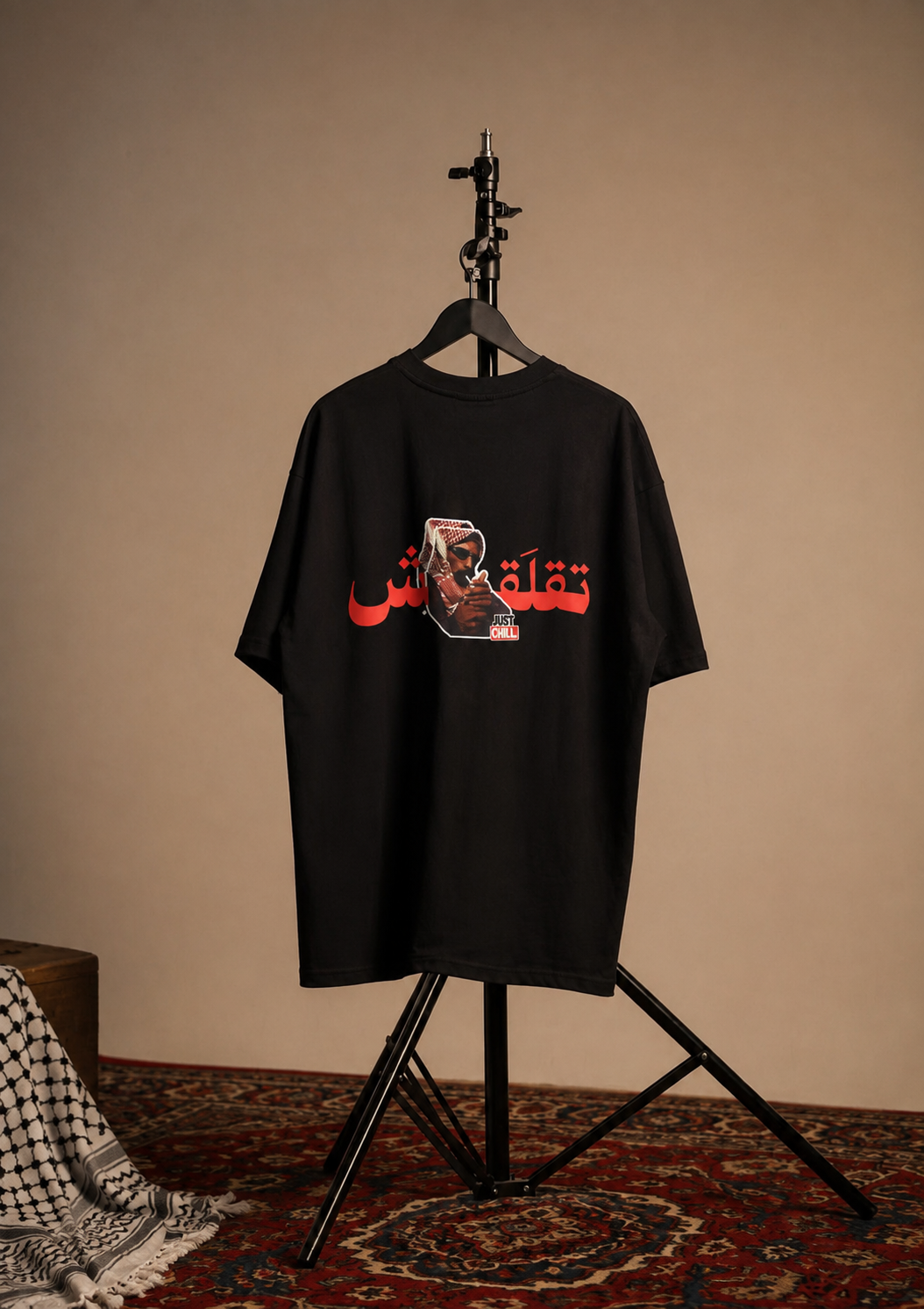 A black short-sleeve graphic T-shirt hanging on a black hanger stand against a beige wall, with a red Arabic text print and a small illustrated graphic across the chest.