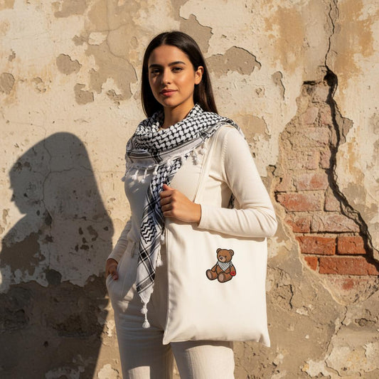 The Mark Tote - street style beautiful young arab woman wearing kuffiyeh on shoulders with one hand in pockets. image for upper half only. background old cracked wall. Minimalist outfit and highlights the bag, design must be visible, captured in sharp focus. Bright afternoon sun.