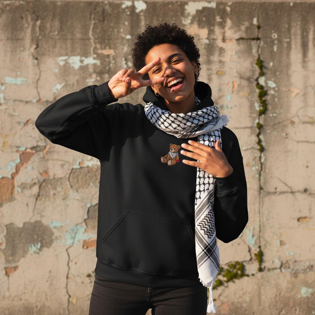 The Ruffalo Hoodie  happy fun arab genz wearing kuffiyeh around neck, in ecstatic mood, making a genz camera pause and raising a victory sign. image for upper half only. background old cracked wall. Minimalist outfit and highlights the design, captured in sharp focus. Bright afternoon sun. design must be visible