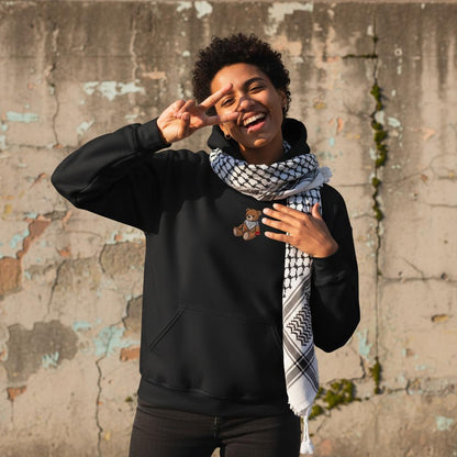 The Ruffalo Hoodie  happy fun arab genz wearing kuffiyeh around neck, in ecstatic mood, making a genz camera pause and raising a victory sign. image for upper half only. background old cracked wall. Minimalist outfit and highlights the design, captured in sharp focus. Bright afternoon sun. design must be visible