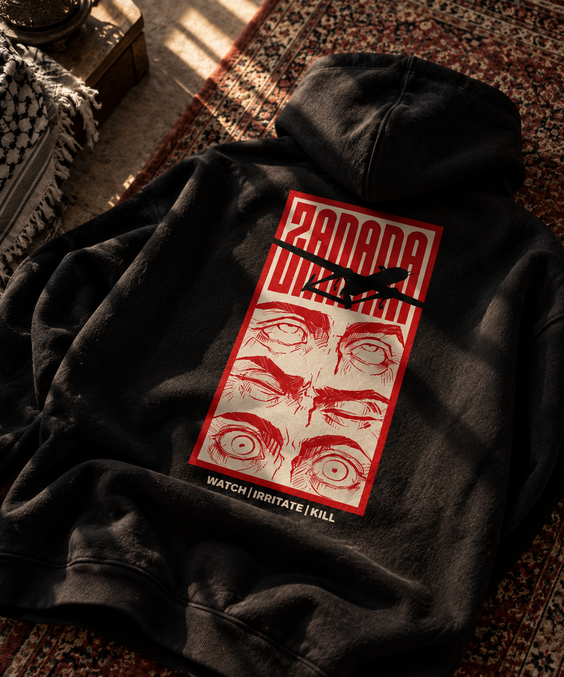 A black hooded sweatshirt laid flat on a patterned rug, showing the back graphic. The print features a red border, stylized red eyes, a black airplane silhouette, and the word 'ZANANA' in red at the top, with smaller text below reading 'WATCH | IRRITATE | KILL'.