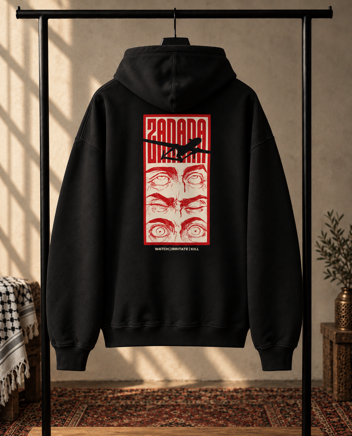 A black pullover hoodie hanging on a black clothing rack in a styled indoor room. The back of the hoodie features a large red graphic print with the word 'ZANANA' at the top, a black bird silhouette across the center, and four stylized faces below.